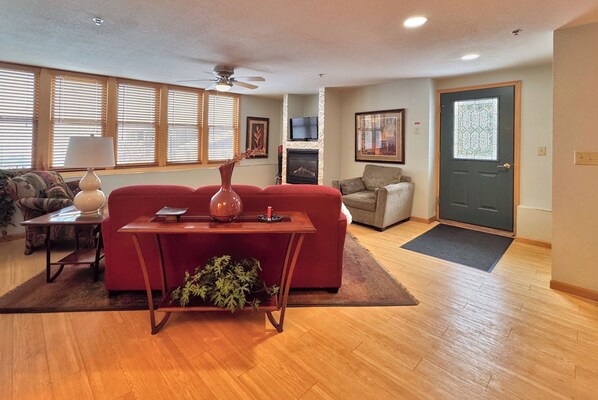 A living room with a red sofa, a wooden coffee table, a fireplace, a television, and a door with a decorative glass panel.