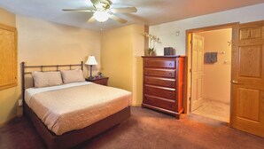 Ein Schlafzimmer mit Bett, Schminktisch, Nachttisch, Deckenventilator und einer Tür zu einem anderen Raum.