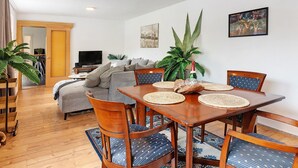 Et spiseområde med et træbord, stole og et fjernsyn i baggrunden.
