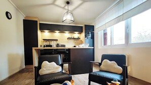 Une cuisine moderne avec des meubles de couleur sombre, un plan de travail en bois et un luminaire suspendu. On y trouve deux chaises avec des coussins blancs et une table sur laquelle sont disposés divers objets.