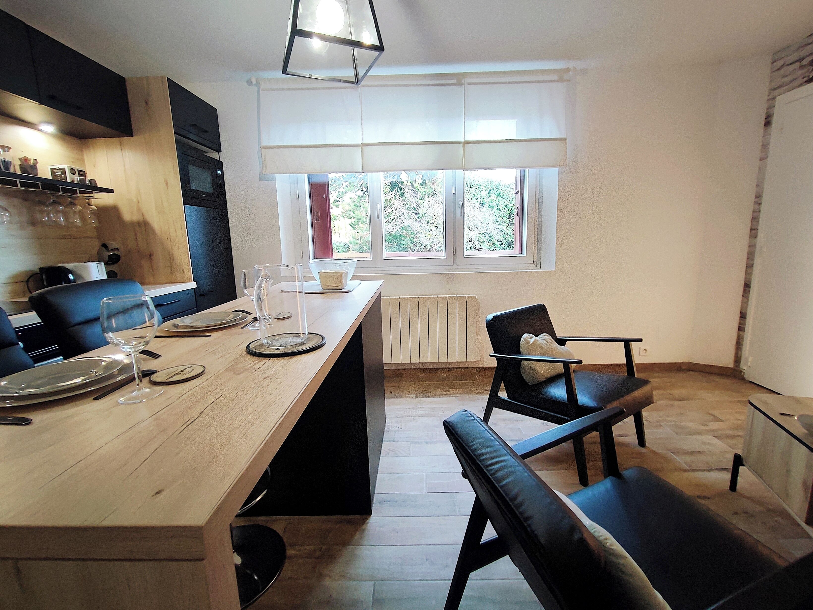 A modern kitchen with a wooden table, black chairs, and a window with blinds.
