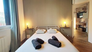 Un lit bien fait, avec des oreillers et des serviettes enroulées, des lampes de chevet, un mur en briques et un téléviseur fixé au mur.