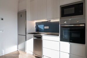 A modern kitchen with stainless steel appliances, including a microwave, oven, and dishwasher, and a built-in sink with a sleek faucet. - GRAN VIA capitals, PRAGA (Madrid)