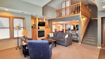 A spacious living room with a fireplace, a staircase to an upper level, and a kitchen area visible through an open door.