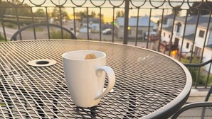 A white mug on a round metal table with a metal railing and a view of a sunset. - Top-Floor Condo | Lake Views | Walk Downtown (Bayfield)