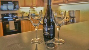 A kitchen with wooden cabinets, a microwave, a stove, and a wine bottle with two glasses. - Top-Floor Condo | Lake Views | Walk Downtown (Bayfield)