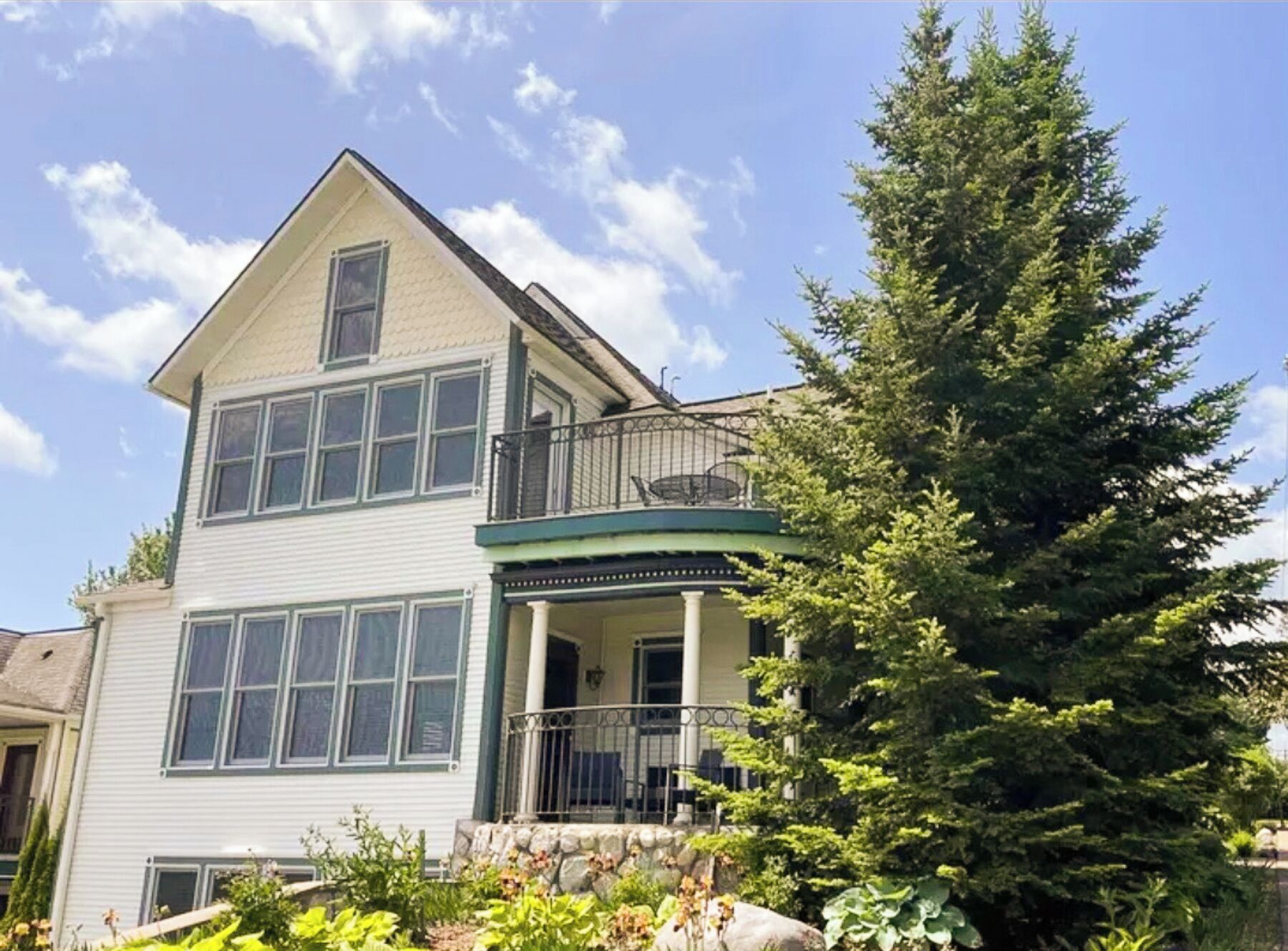 A two-story house with a balcony, large windows, and a stone foundation.