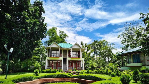 A two-story building with a green roof, surrounded by well-maintained gardens and trees. - Hotel Dynasty Inn (Mal)