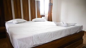 A neatly made bed with white linens and pillows, a wooden headboard, and a window with curtains. - Hotel Dynasty Inn (Mal)
