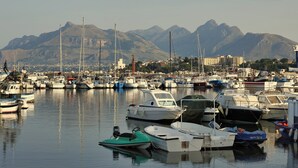 Un port de plaisance avec des bateaux amarrés, une grue en arrière-plan et des montagnes à l’horizon.