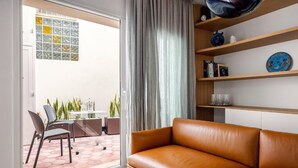 Un salon moderne avec un canapé en cuir, une table en verre, des chaises et une vue sur un jardin, accessible par une porte-fenêtre coulissante.