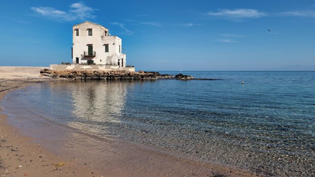 Un bâtiment blanc doté d’un balcon, situé sur une côte rocheuse au bord de la mer.