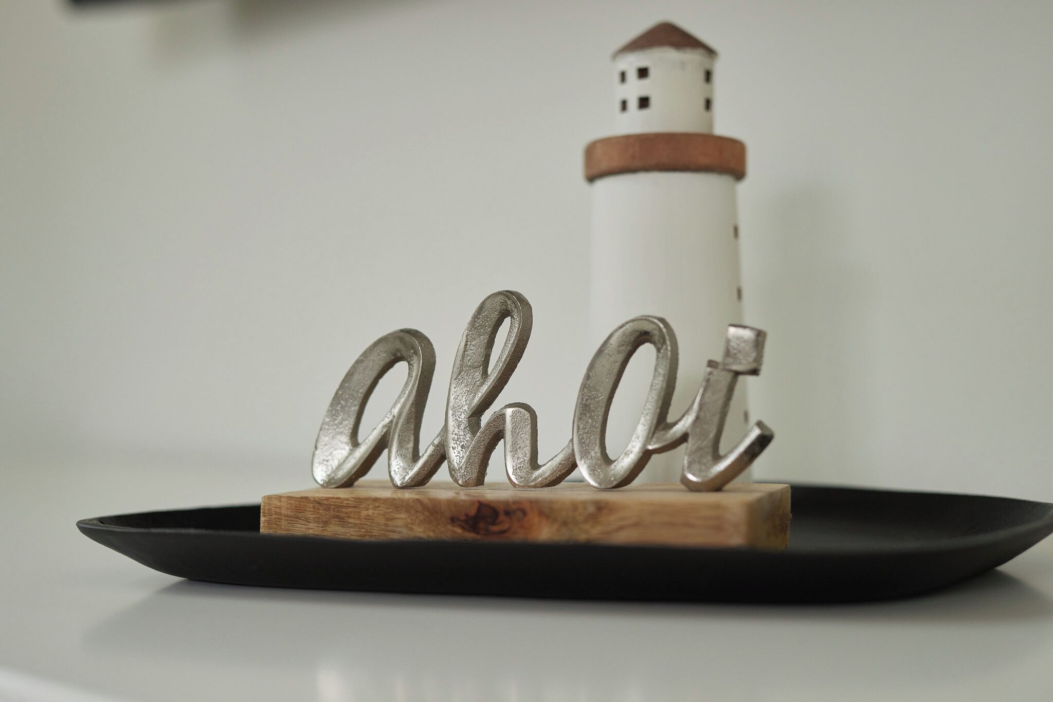 Un letrero metálico decorativo que dice “ahot” sobre una base de madera, con un faro al fondo.