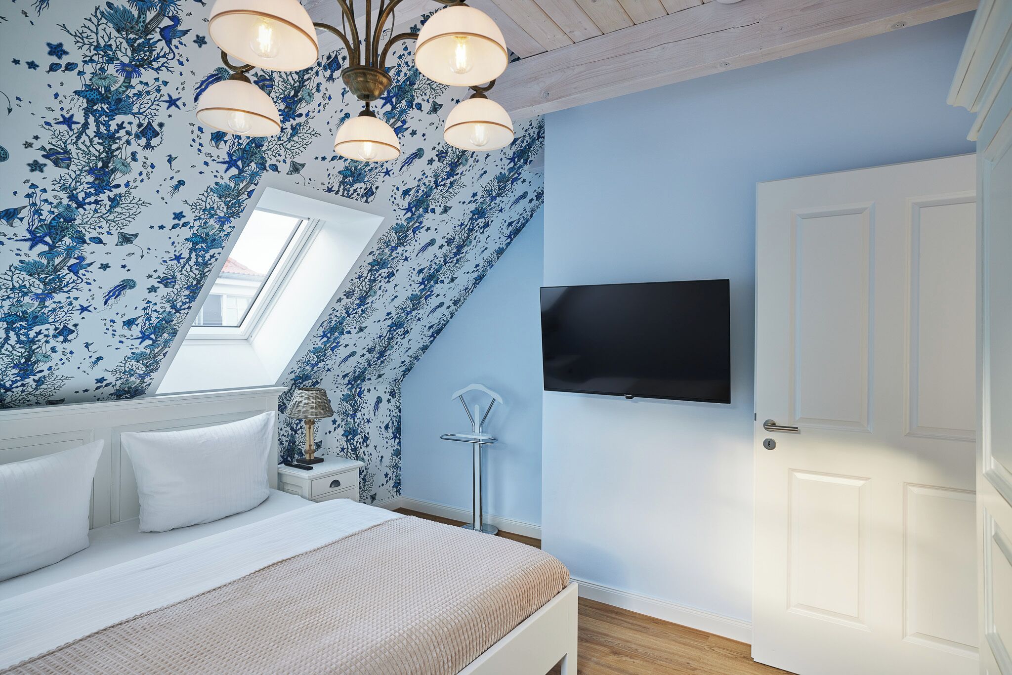 Une chambre à coucher avec un lit, un téléviseur fixé au mur, une porte et une lucarne.