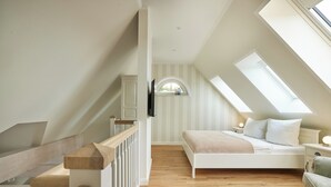 A bedroom with a sloped ceiling, a bed, a nightstand, a chair, and a window.