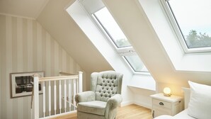 Une chambre avec un plafond en pente, un fauteuil à capitons, une table de chevet avec une lampe et un tableau encadré au mur.