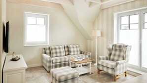 Un salon avec un canapé à carreaux, un fauteuil, un pouf et une petite table sur laquelle se trouve une lampe.