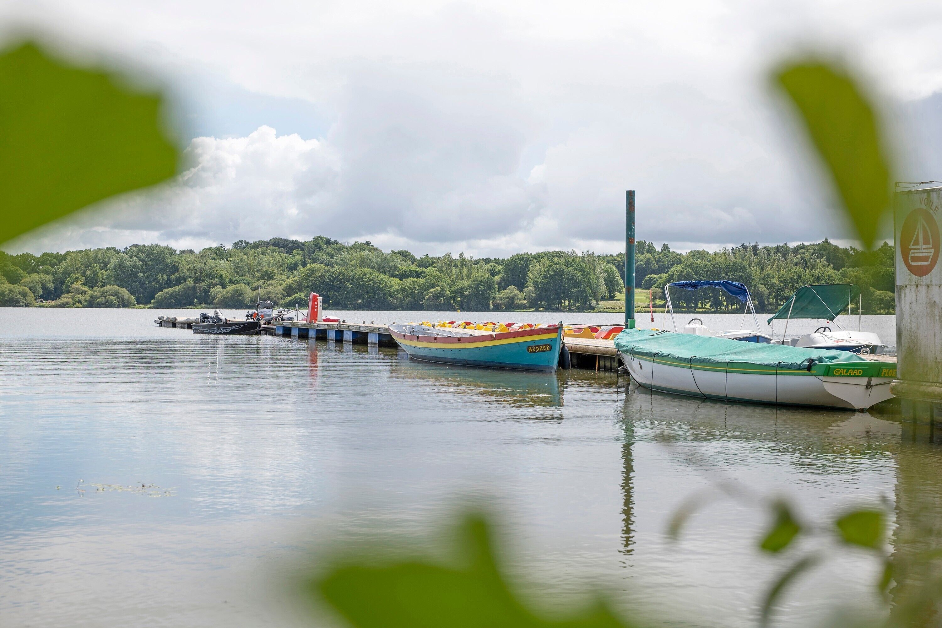Un lac paisible où des bateaux sont amarrés à un quai, le tout entouré d’une végétation luxuriante.