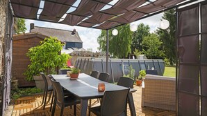 Eine Terrasse im Freien mit Tisch und Stühlen, umgeben von Topfpflanzen und einer Pergola.