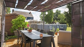 Un patio al aire libre con una mesa y sillas, rodeado de plantas en macetas y una pérgola.