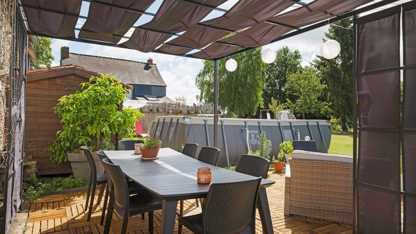 An outdoor patio with a table and chairs, surrounded by potted plants and a pergola.