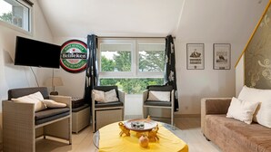 Ein Wohnzimmer mit Rattanmöbeln, einem Flachbildfernseher, dem Heineken-Logo und gerahmten Bildern an der Wand.