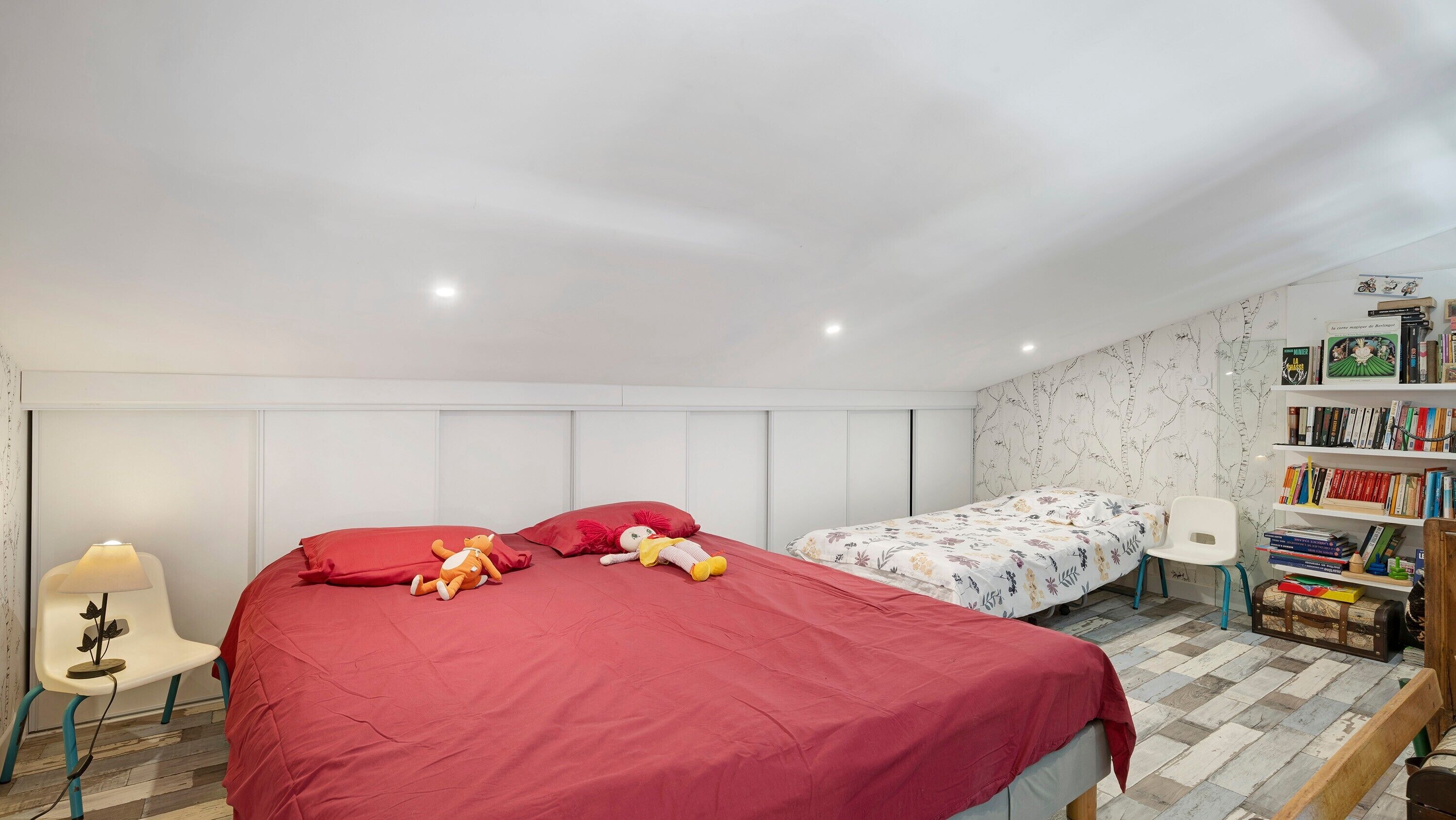 A bedroom with a large bed, a smaller bed, a chair, a desk, and a bookshelf.