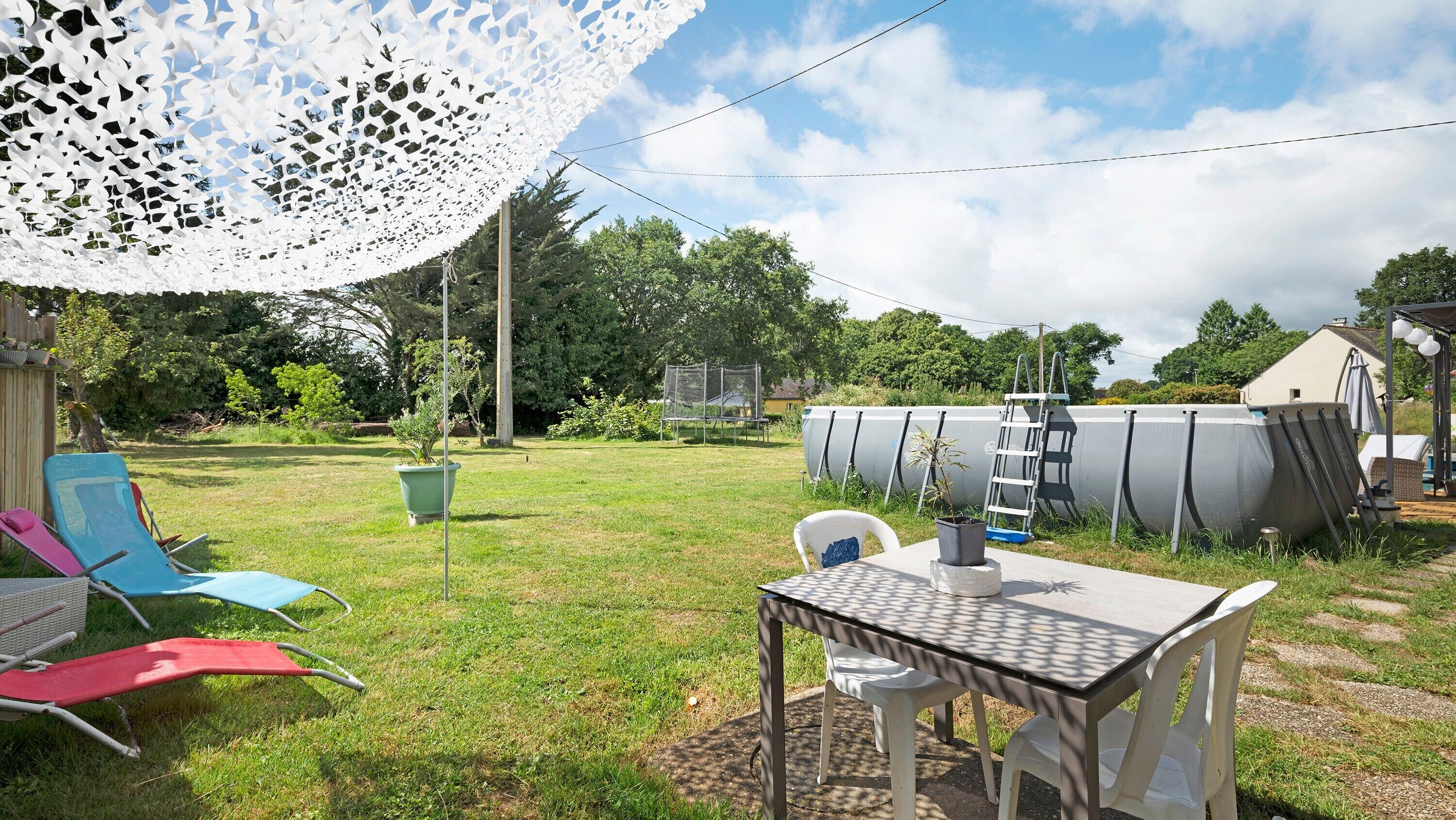 Ein Garten mit Tisch und Stühlen, einem weißen Spitzbogenvorzelt und einem Swimmingpool im Hintergrund.
