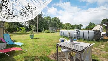 Ein Garten mit Tisch und Stühlen, einem weißen Spitzbogenvorzelt und einem Swimmingpool im Hintergrund.