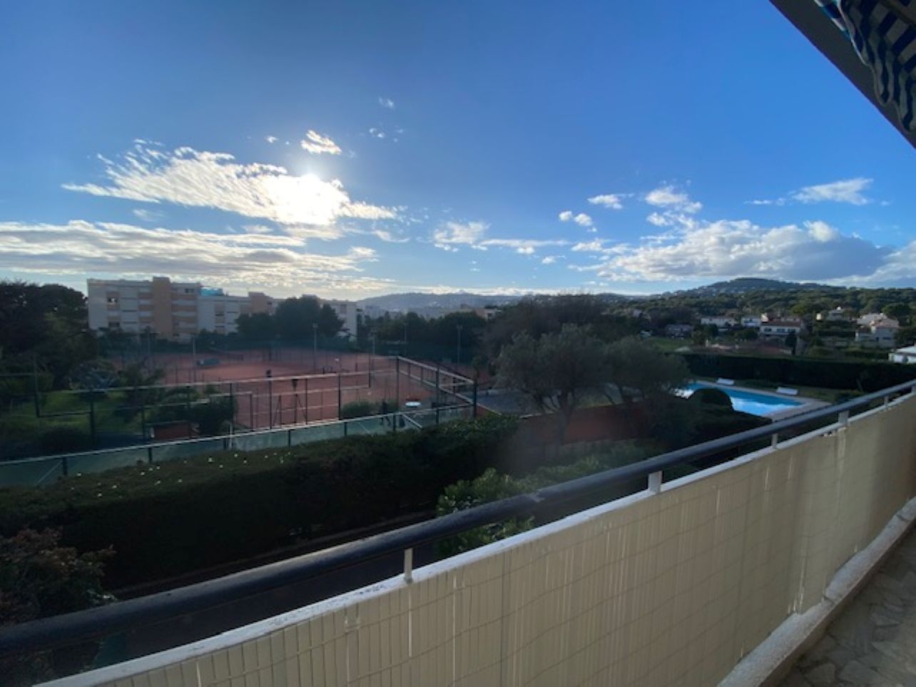 Vista desde un balcón con tenis, piscina y edificios al fondo.