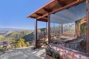 Un espace extérieur abrité, doté d’une table et de chaises, d’un sol en pierre et offrant une vue sur les collines.