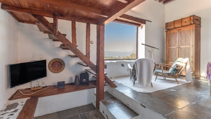 Un escalier en bois mène à un balcon où se trouvent un téléviseur, une chaise et un meuble.