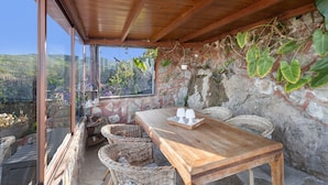 Une table en bois, deux tasses blanches, des chaises en osier et un mur de pierre orné de plantes grimpantes.