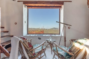 A room with a large window, wooden furniture, a telescope, and a small table with a vase.