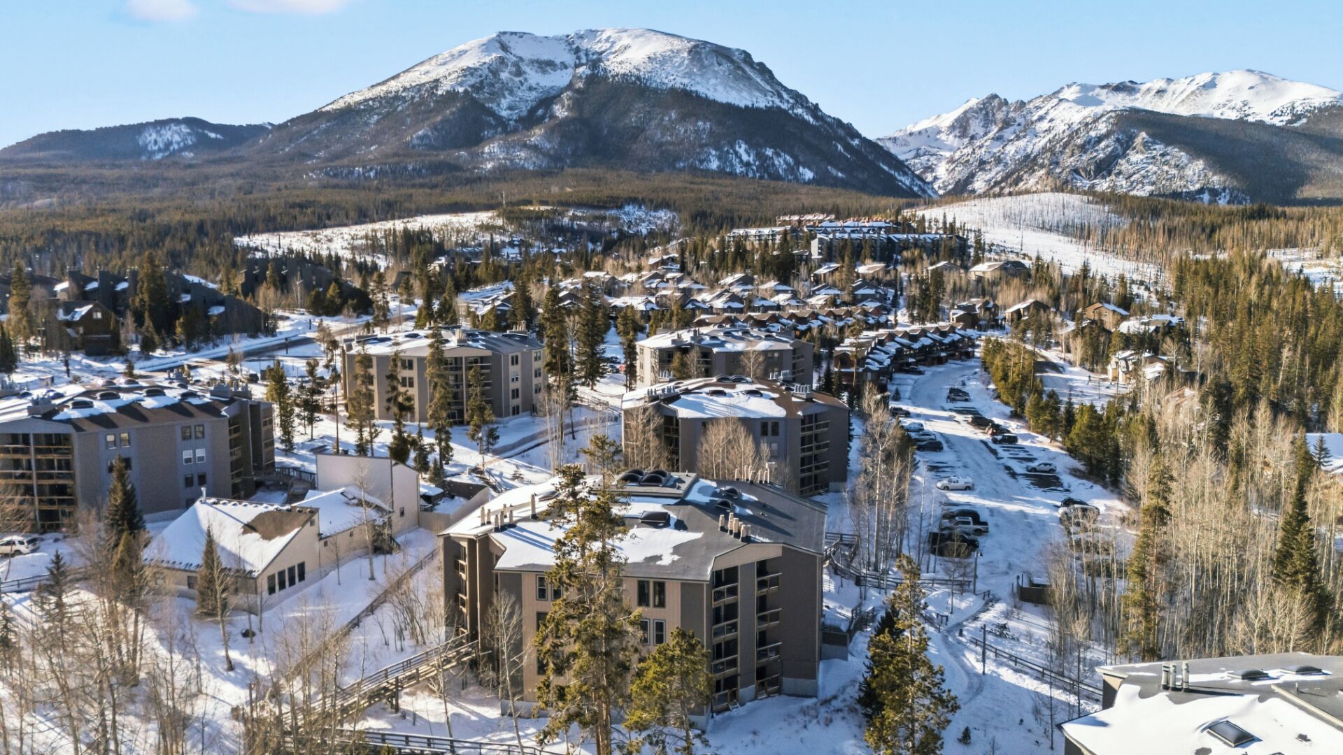 A snow-covered town with modern buildings, a ski resort, and mountains in the background.