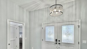 A hallway with a chandelier, double doors with frosted glass panels, and a wooden floor. - Twilight Mist - 3/2 in The Village of Poinciana (Poinciana, The Villages)