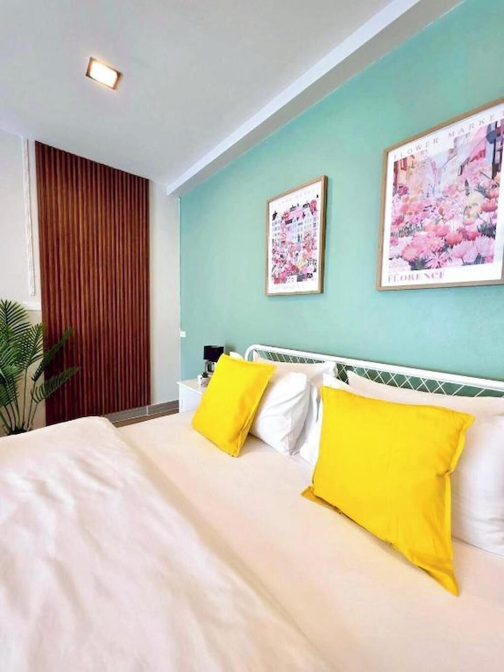 Een hotelkamer met een bed, twee kussens, een nachtkastje, een lamp en een muur met twee ingelijste foto's.
