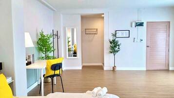 Een hotelkamer met een bed, een bureau, een stoel en een bijzettafeltje. Er staan planten in de kamer en een deur is zichtbaar.
