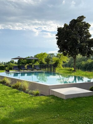 A swimming pool with lounge chairs and a pergola, surrounded by lush greenery and a large tree.