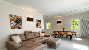 A modern living room with a sectional sofa, a dining area with a table and chairs, and artwork on the walls.