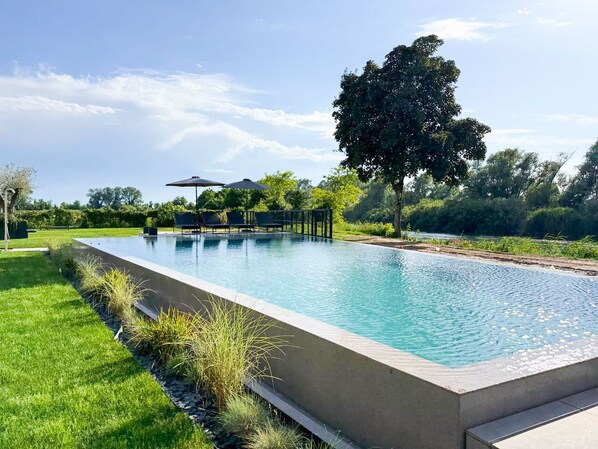 A rectangular swimming pool with a clear blue water surface, surrounded by a well-maintained grassy area and a few trees.