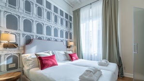 A hotel room with a large bed, two bedside tables, a mirror, and a view of a building through the window. - Design Florence Suite with large terrace (Firenze)