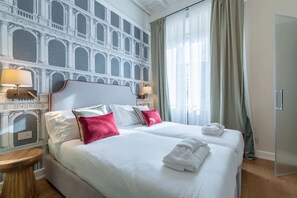 A hotel room with a large bed, two bedside tables, a mirror, and a view of a building through the window. - Design Florence Suite with large terrace (Firenze)