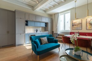 A modern kitchen with grey cabinets, a teal sofa, and a dining area with red chairs. - Design Florence Suite with large terrace (Firenze)