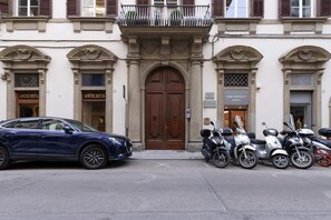 A building with a central entrance, two shops on either side, and a parked car and scooters in front. - Design Florence Suite with large terrace (Firenze)