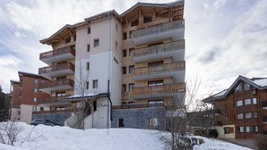 Un hotel de diverses plantes amb balcons, façana de pedra i un paisatge nevós.