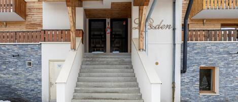 A hotel entrance with a wooden facade, a stone wall, and a staircase leading to the doors.