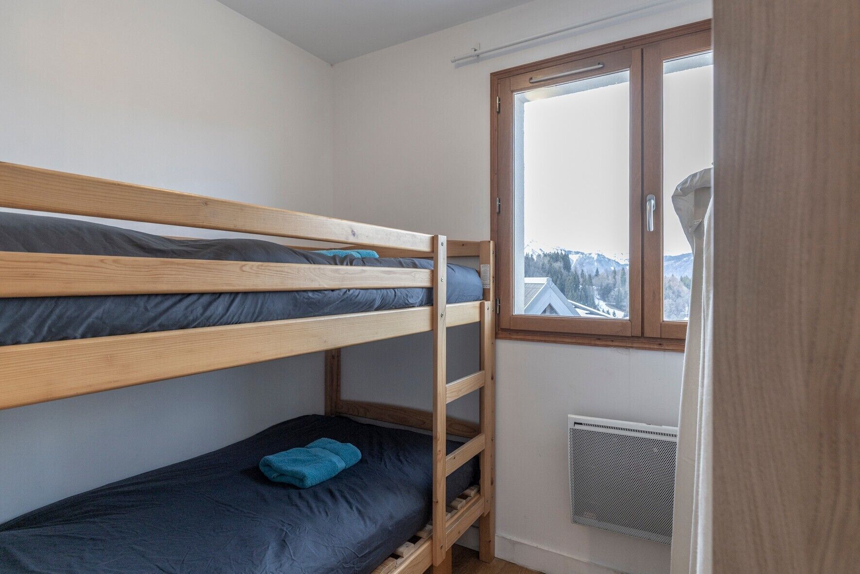Een slaapkamer met stapelbed en een raam dat uitkijkt op een besneeuwd landschap.