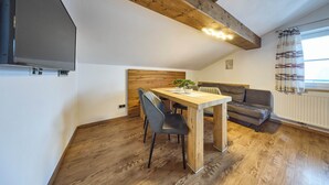 A cozy room with a wooden dining table, two chairs, a sofa, and a window with curtains. - Apartment Wenger Leogang (Leogang)