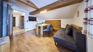 A modern living space with a wooden ceiling, a dining area with a table and chairs, and a gray sofa. - Apartment Wenger Leogang (Leogang)